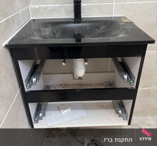 כיור שחור עם ברז, צנרת וכלים על הרצפה